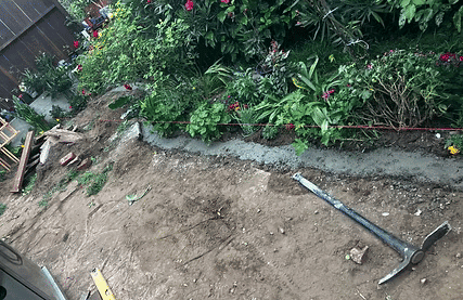 Garden landscaping project in progress, featuring soil, plants, and freshly poured concrete.