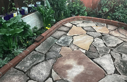 Stone patio with irregular flagstone, bordered by brick and surrounded by lush greenery.