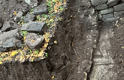 Soil with stones and bricks, surrounded by fallen leaves on a pathway.