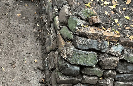 Ancient stone wall with moss in a natural setting surrounded by dirt.